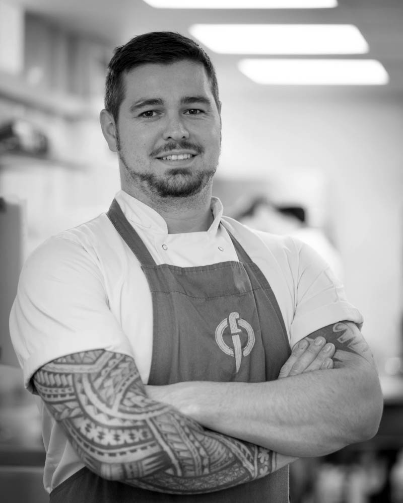 Fletcher Andrews, head chef and owner of Fletcher's Restaurant, Plymouth, dressed in chef's whites and standing proudly in his kitchen.