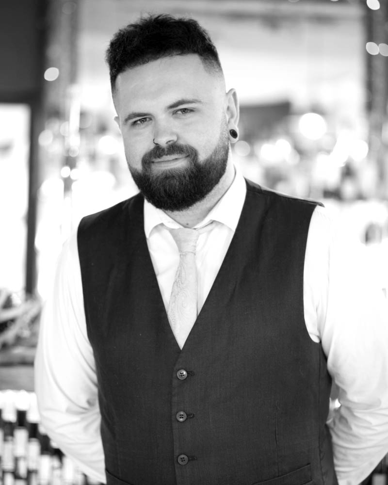 Meet Adam, the Head Waiter at Fletcher's Restaurant, standing in the dining area, ready to ensure every guest has a fantastic dining experience.